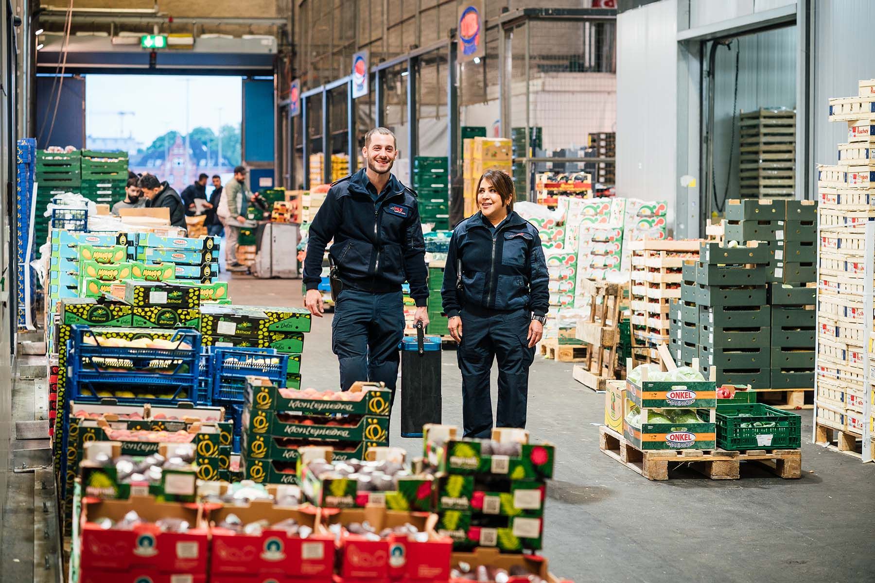 Zwei Mitarbeiter auf dem Großmarkt Hamburg mit Geldkoffer zwischen Obst- und Gemüsekisten