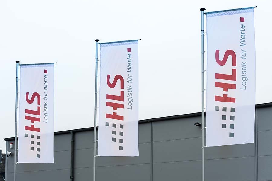 Drei Fahnen mit Firmen-Logo vor Gebäude